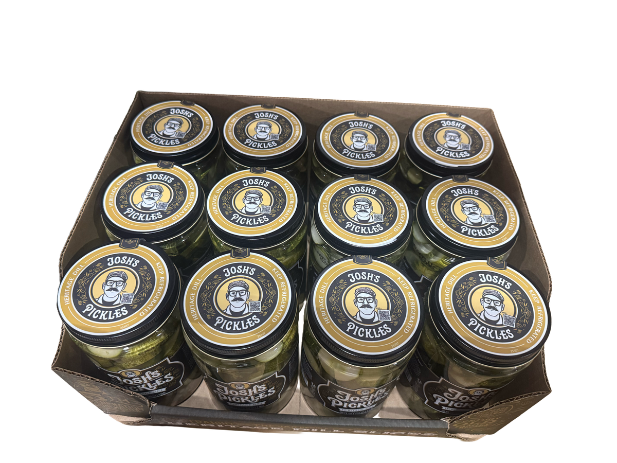 Overhead view of twelve Josh’s Pickles Heritage Dill Slices 35 fl oz jars arranged in three rows of four in a Costco display tray, with branded lids visible.
